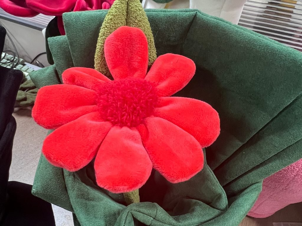 Red plush flower bouquet wrapped in green fabric showing soft plush petals and bendable stem design